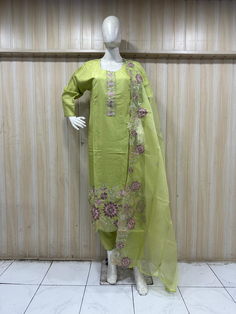 mannequin waering a green embroidered outfit with floral dupatta against a striped wall