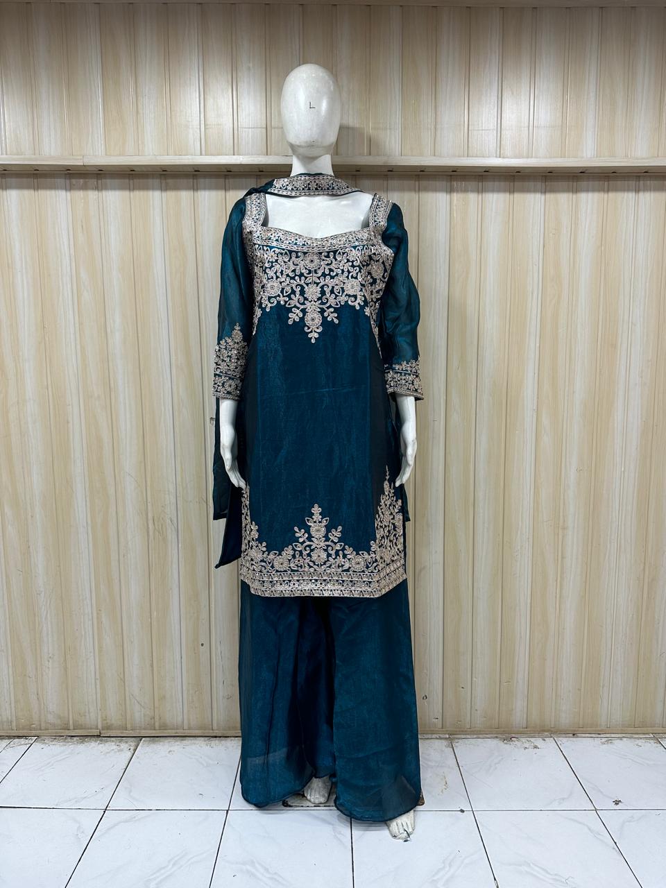 mannequin wearing teal embroidered traditional outfit with a patterns against a striped wall
