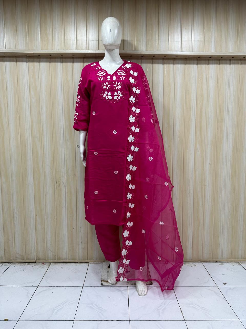 Mannequin wearing a magenta traditional outfit with white floral patterns against a striped
