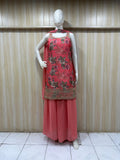 Mannequin wearing a coral pink traditional outfit with floral embroidery against a wooden panel background.