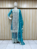 Teal embroidered traditional outfit on a mannequin against a wooden panel background