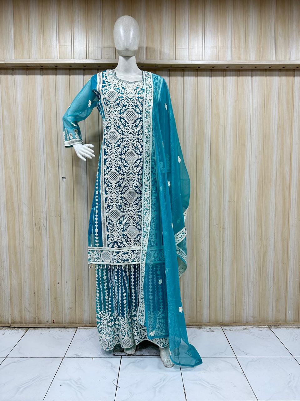Teal embroidered traditional outfit on a mannequin against a wooden panel background