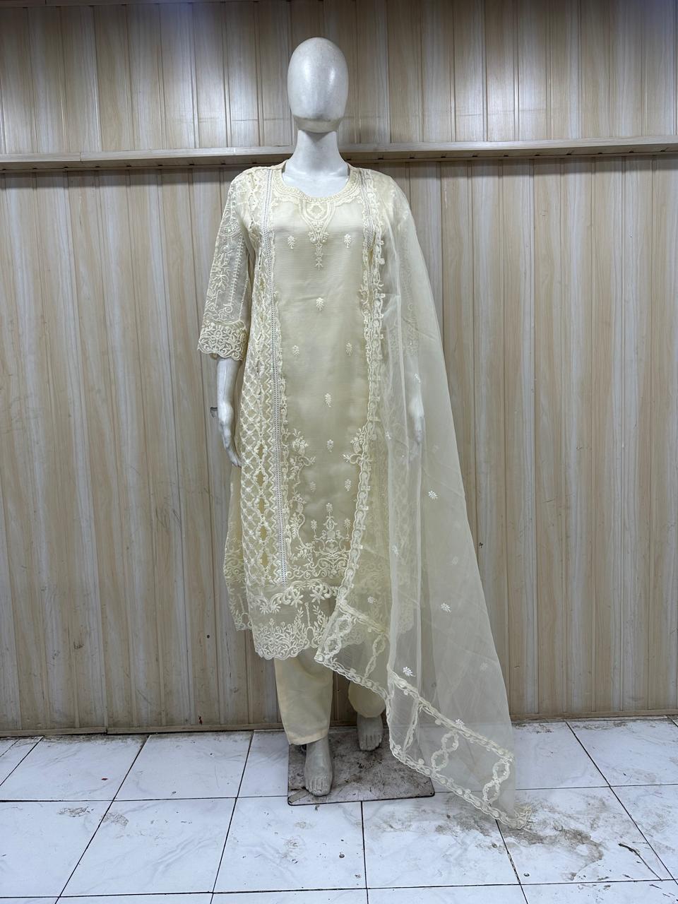 Mannequin wearing a light-colored embroidered outfit with a sheer dupatta against a striped