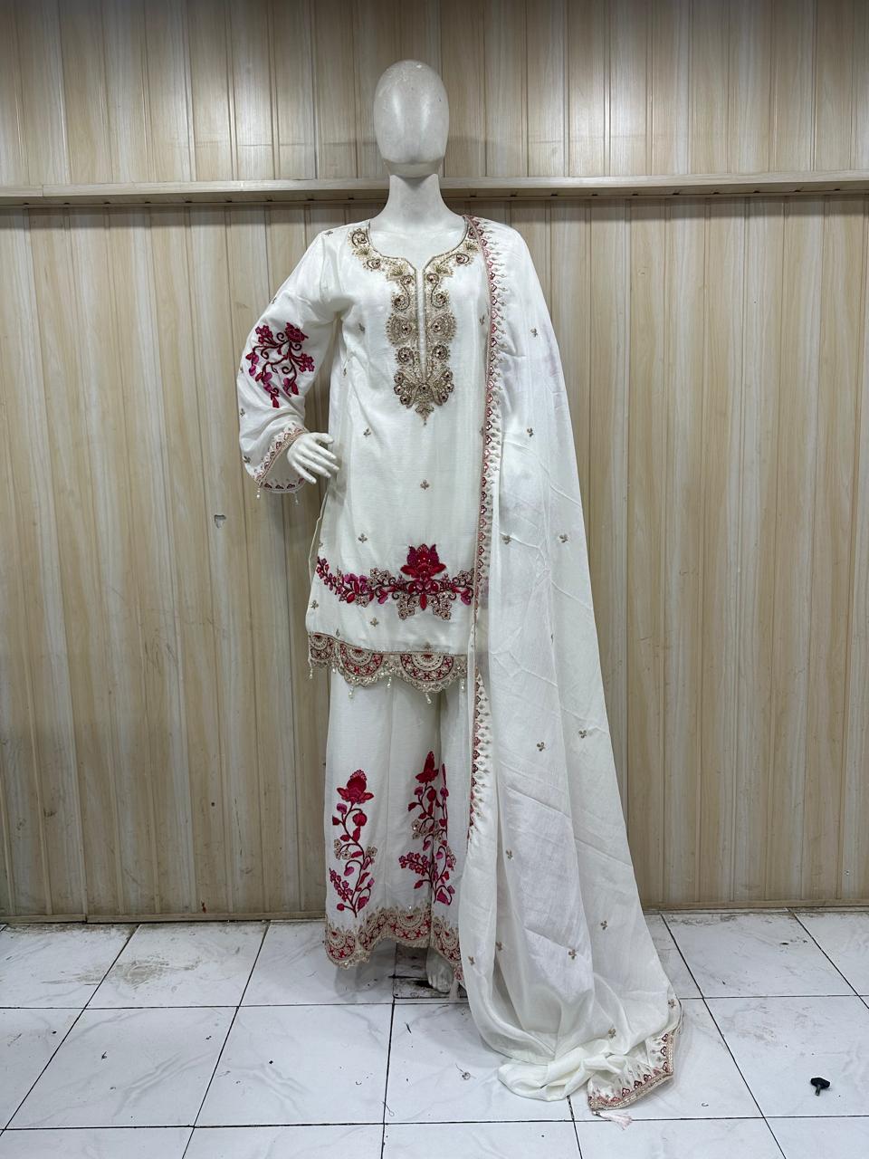 White embroidered traditional outfit with red details on a mannequin against a striped
