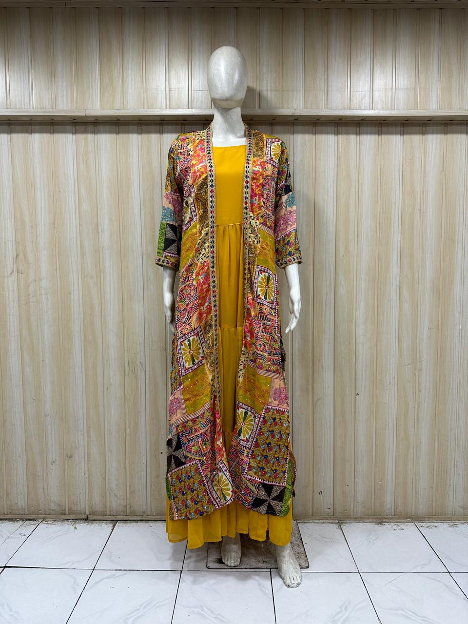 Long Patterned Coat oveMannequin wearing a colorful patterned jacket over a yellow dress against a wooden panel background.r Dark Outfit