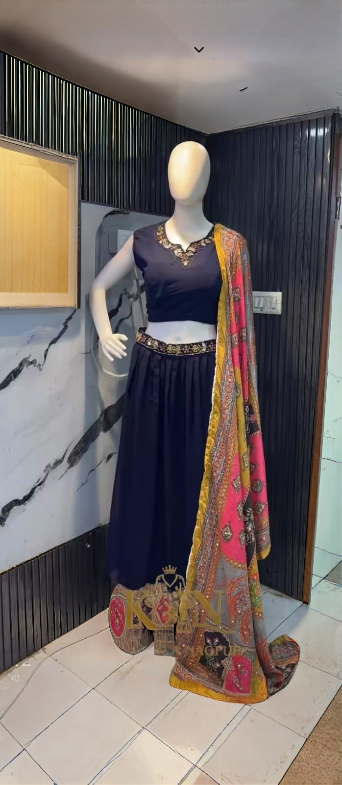Mannequin wearing a traditional outfit with a dark blue dress and colorful dupatta against a marble  ChatGPT2:29 PM