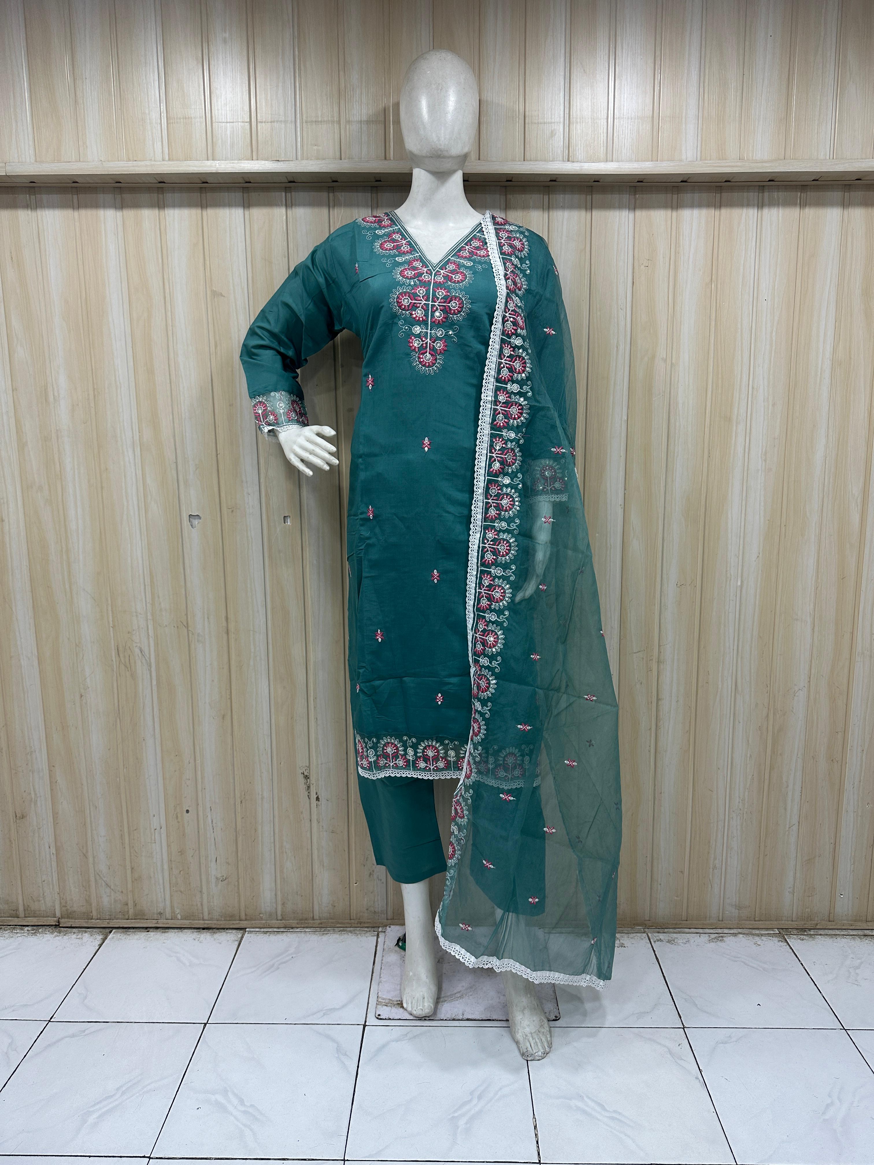Green embroidered traditional outfit on a mannequin against a wooden panel background