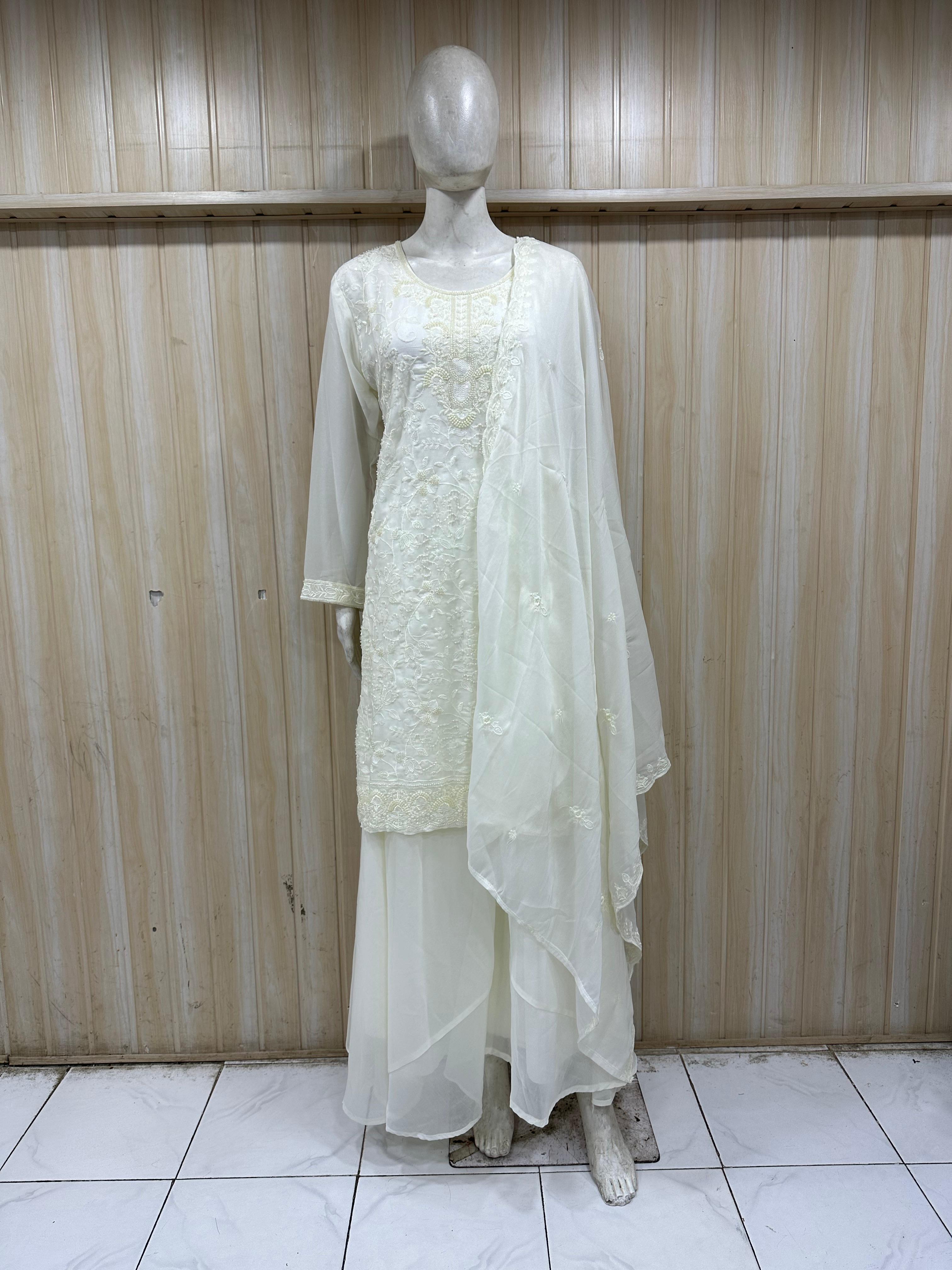 Mannequin wearing a white traditional outfit with a sheer dupatta against a wooden panel background.