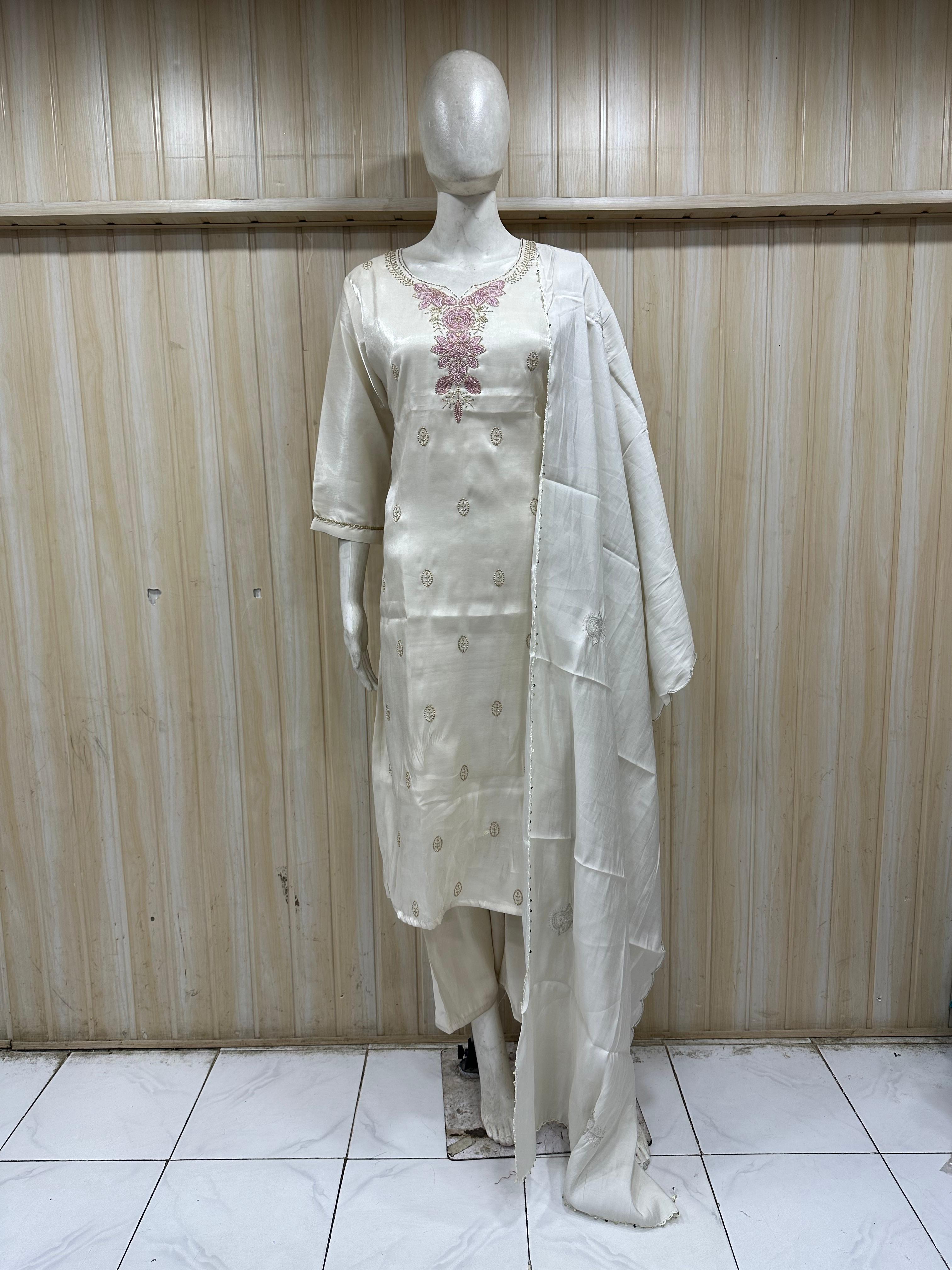 Mannequin wearing a white traditional outfit with a sheer dupatta against a wooden panel background.