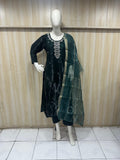 Mannequin wearing a dark green outfit with a matching dupatta against a wooden panel background