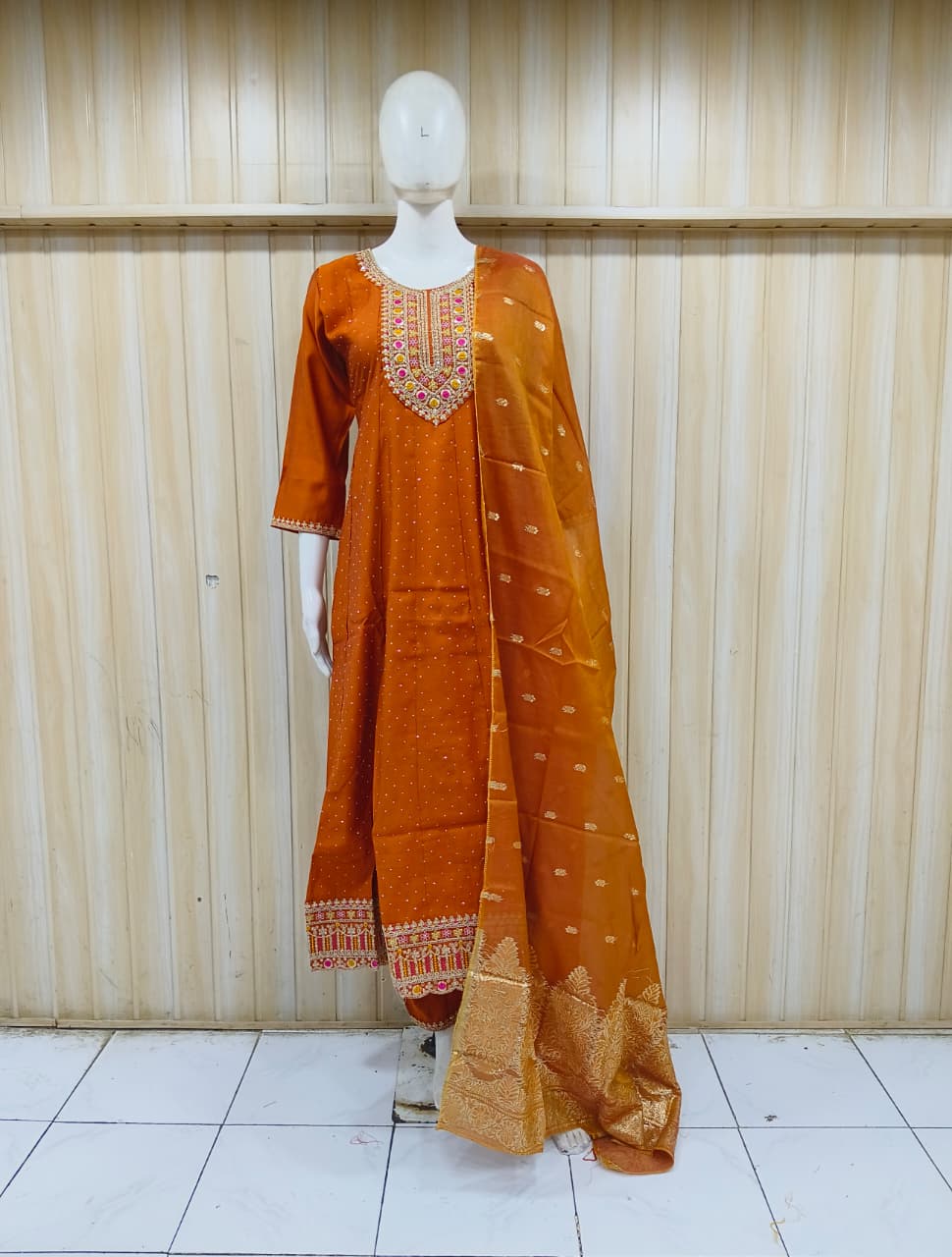 Orange traditional outfit with embroidery on a mannequin against a striped
