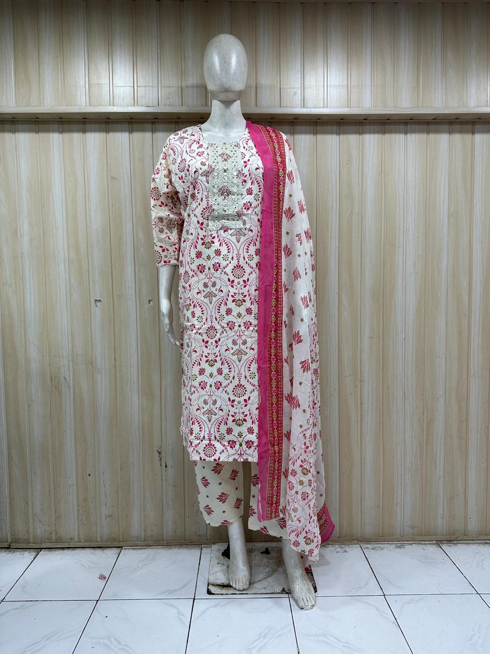 Mannequin wearing a white kurta with red floral patterns and a matching dupatta against a wooden panel background.