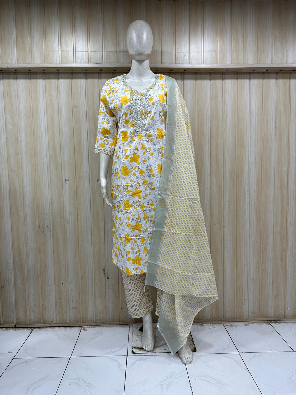 Mannequin wearing a yellow floral dress with a green dupatta against a wooden panel background.