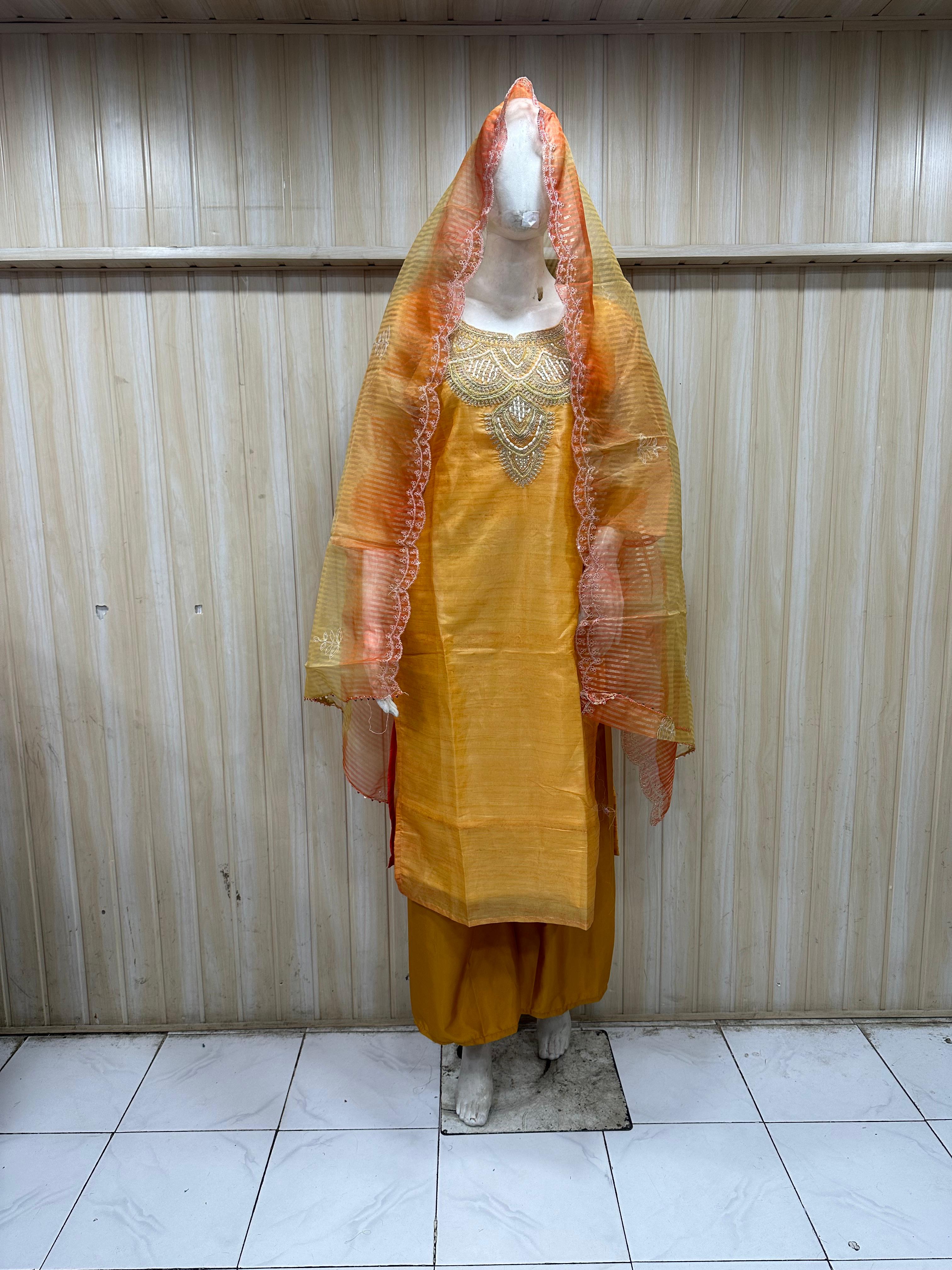 Yellow traditional outfit with an orange dupatta on a mannequin against a striped