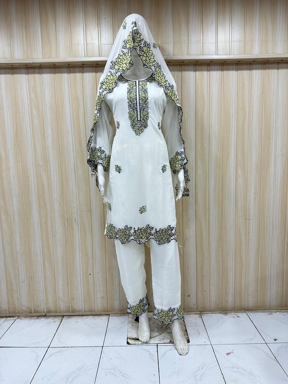 White traditional outfit with green embroidery on a mannequin against a striped
