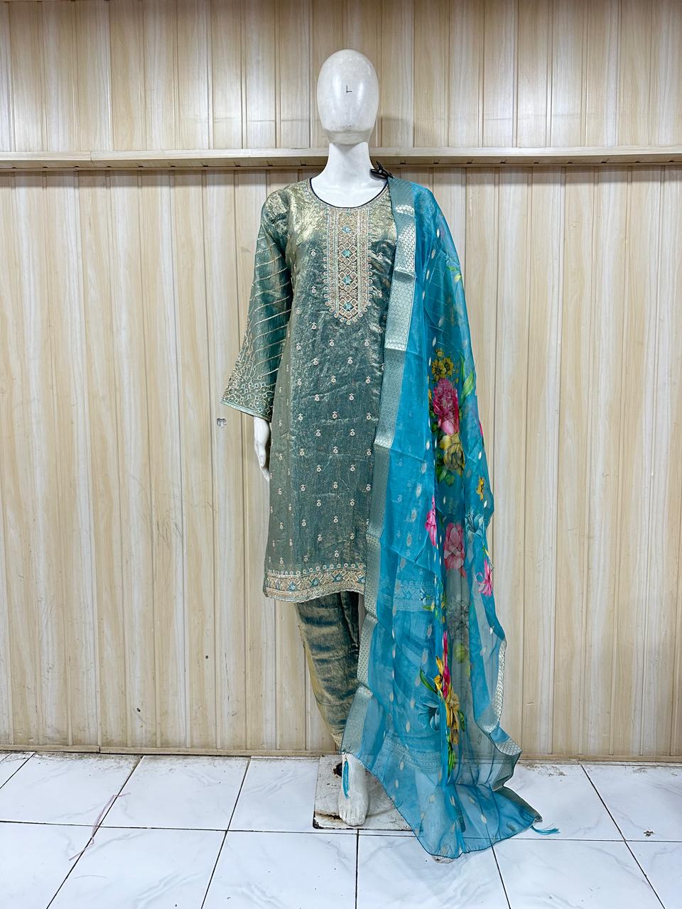 Mannequin wearing a green embroidered outfit with a blue dupatta against a wooden panel background