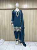 Mannequin wearing a blue embroidered outfit with floral patterns against a wooden panel background.