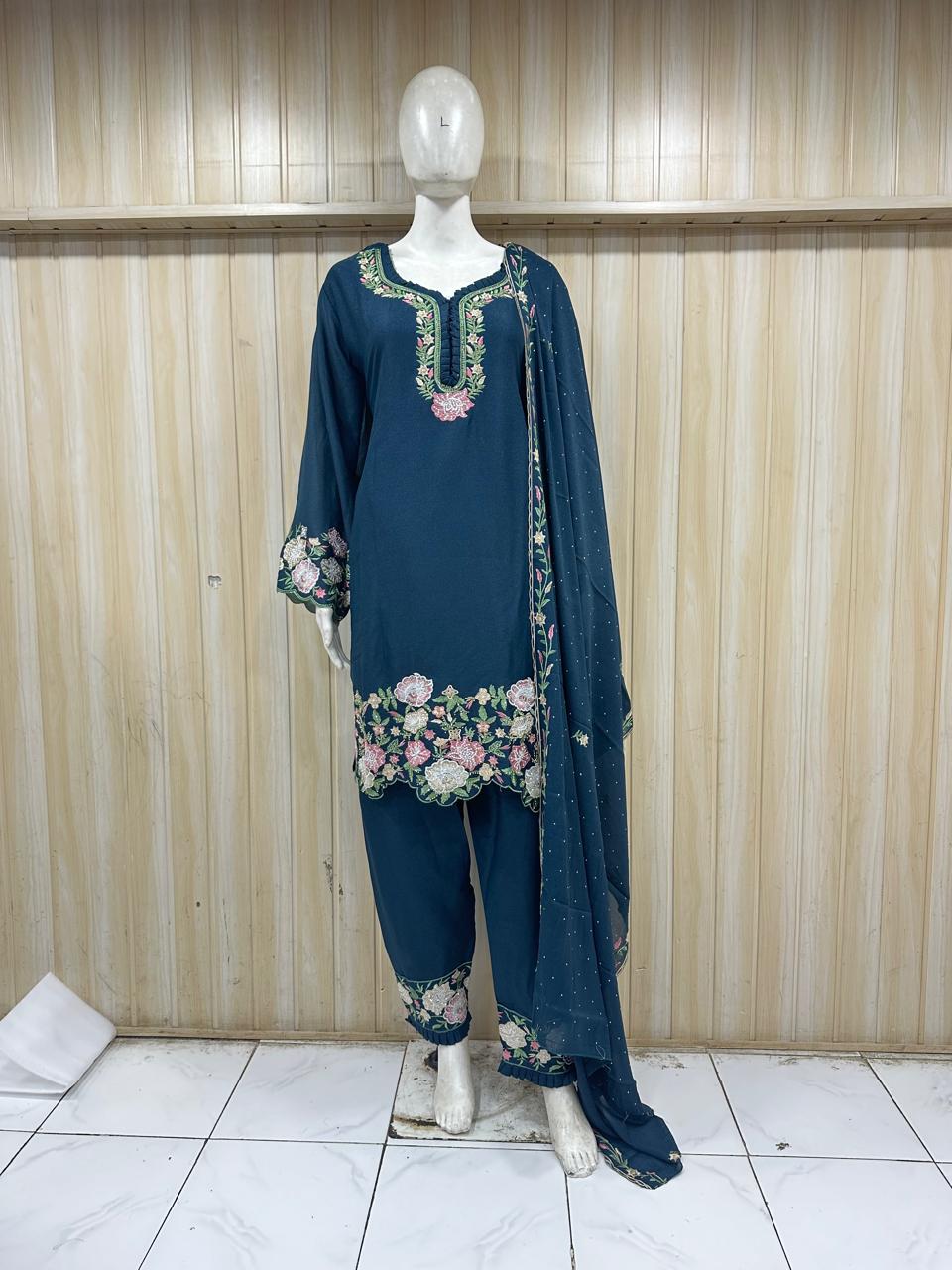 Mannequin wearing a blue embroidered outfit with floral patterns against a wooden panel background.