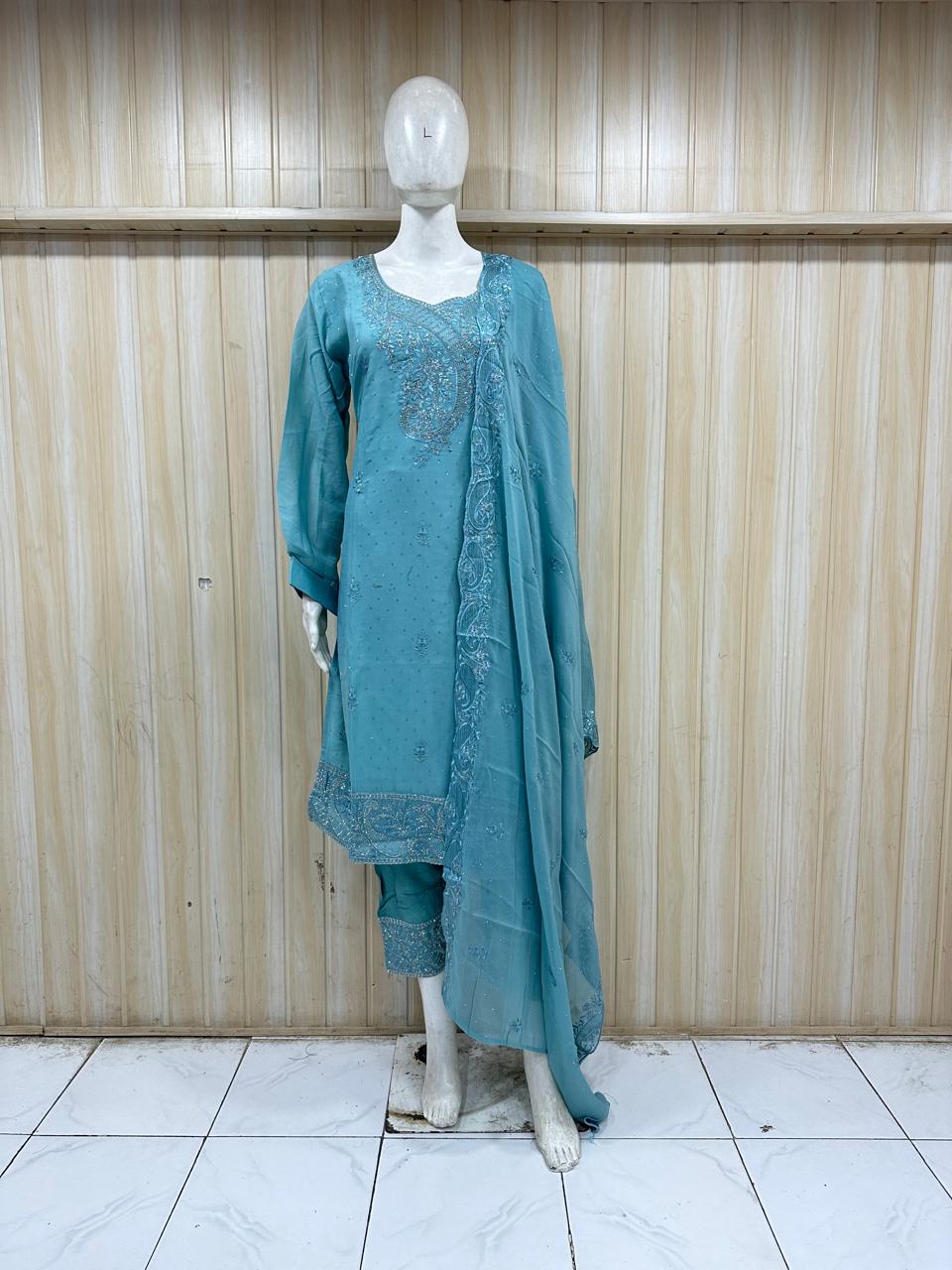 Teal embroidered outfit on a mannequin against a wooden panel background