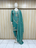 Teal embroidered traditional outfit on a mannequin against a wooden panel background