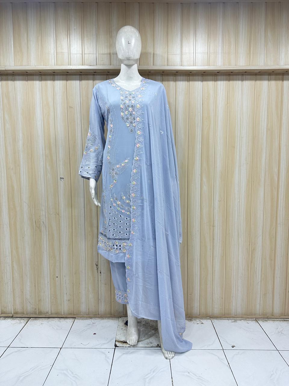 Mannequin wearing a light blue embroidered outfit against a wooden panel background