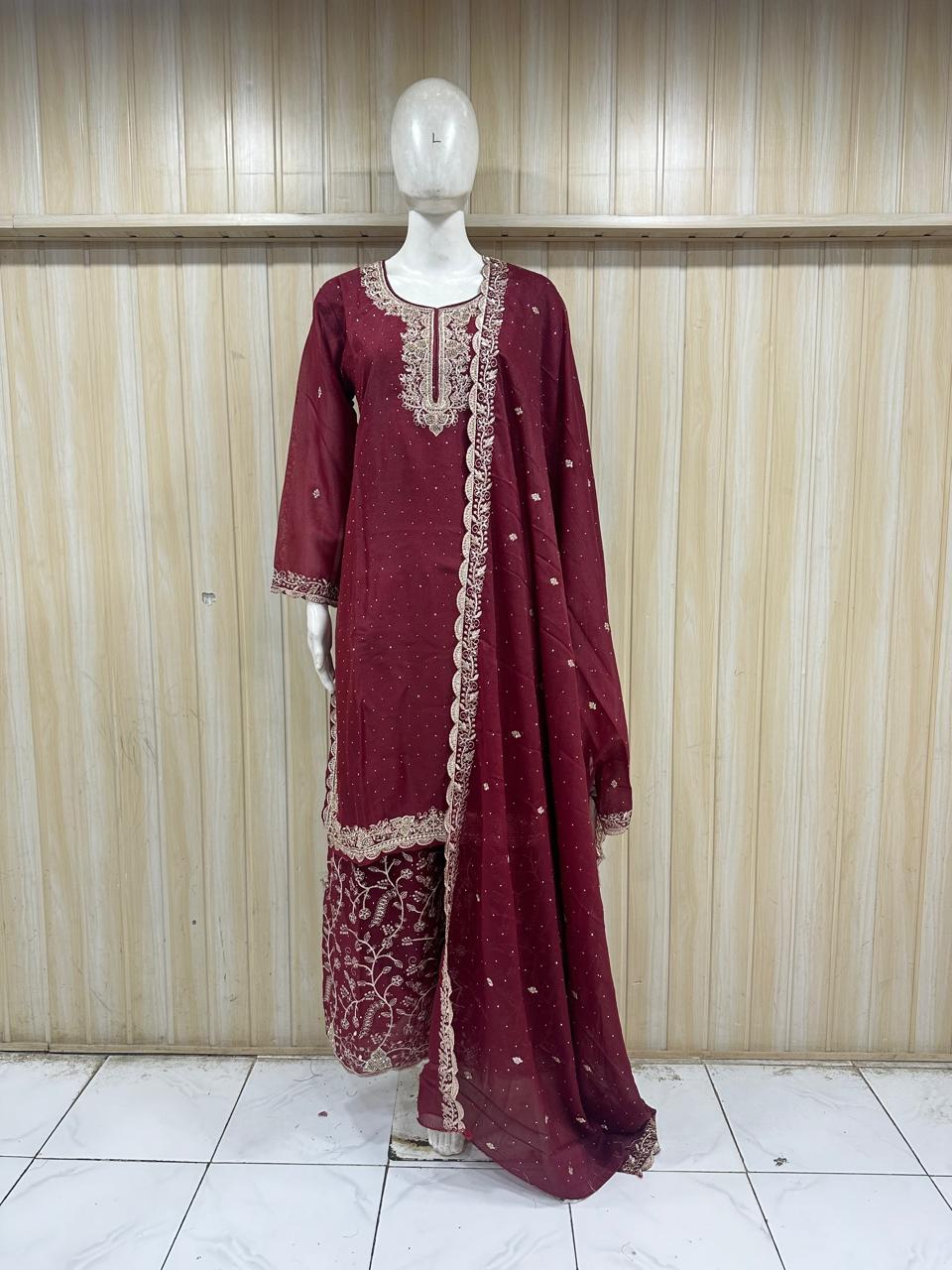 Maroon traditional outfit with intricate patterns on a mannequin against a striped