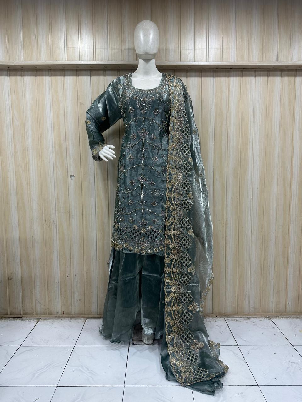 Mannequin wearing a dark green embroidered outfit against a wooden panel background