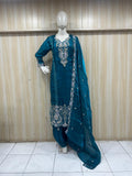 Teal traditional outfit with silver embroidery on a mannequin against a wooden panel background.
