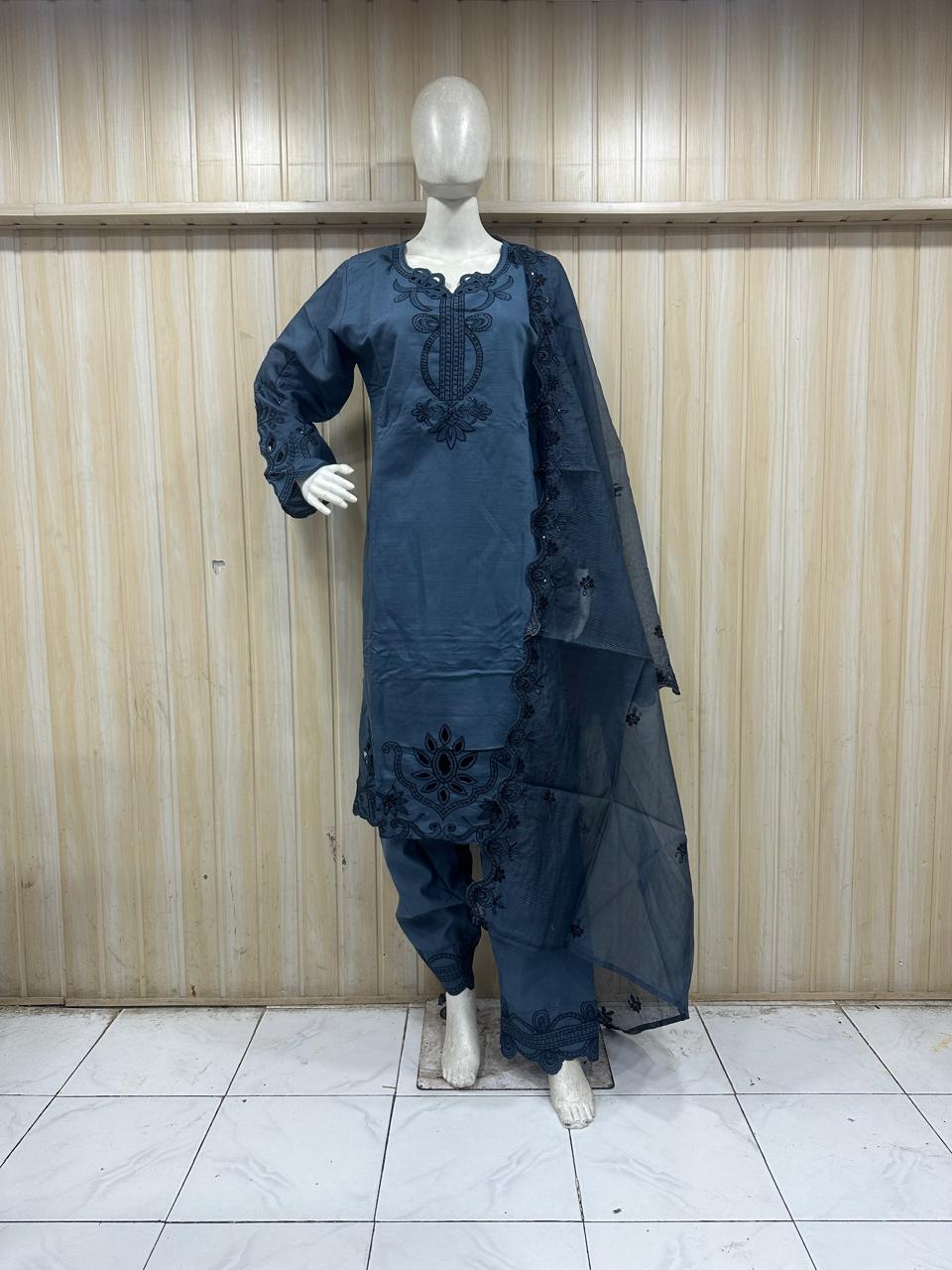 Mannequin wearing a blue embroidered outfit against a wooden panel background