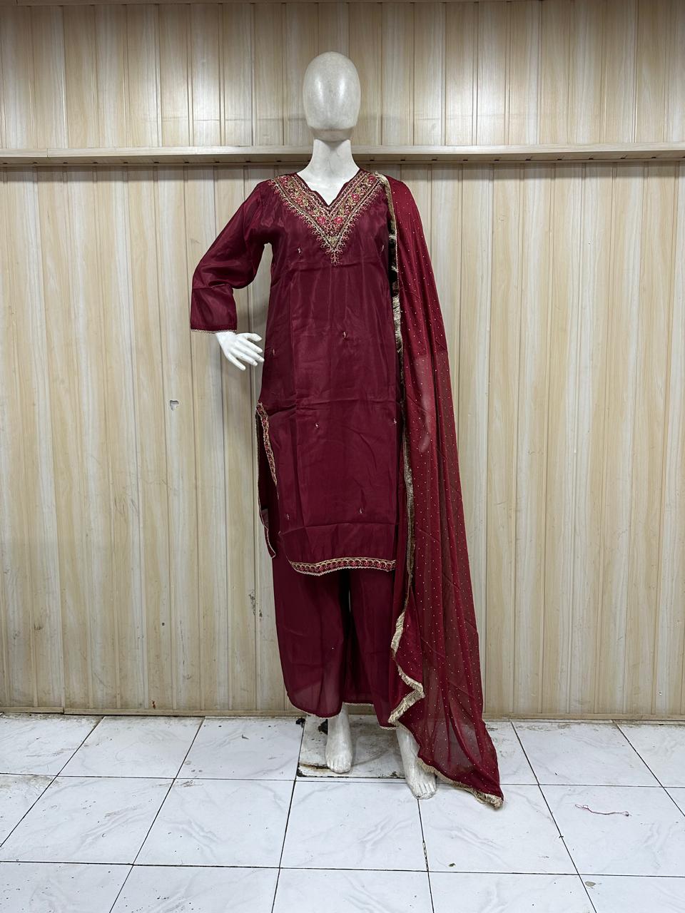 Maroon traditional outfit with intricate patterns on a mannequin against a striped