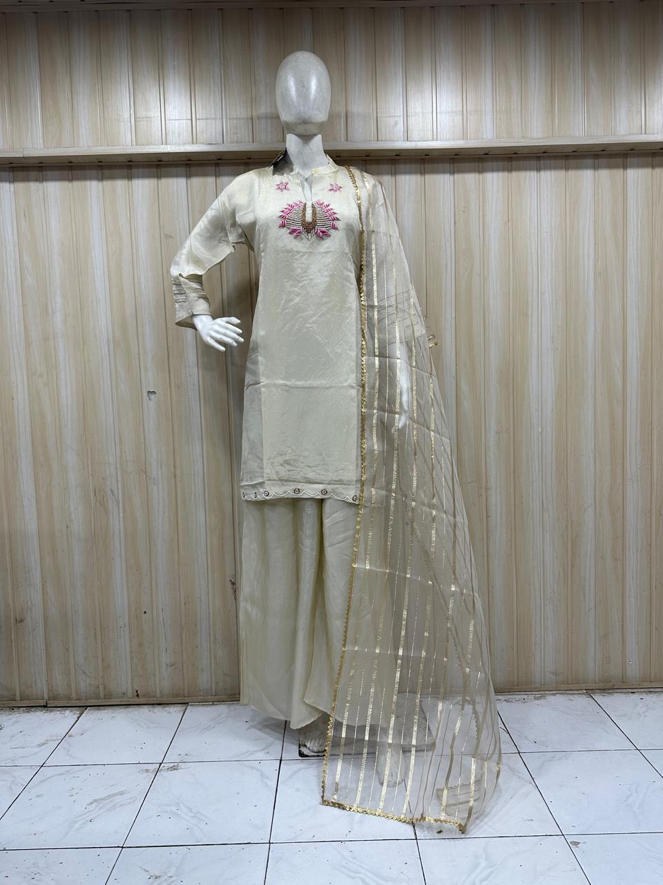 Mannequin wearing a cream-colored traditional outfit with a floral design against a wooden panel background.