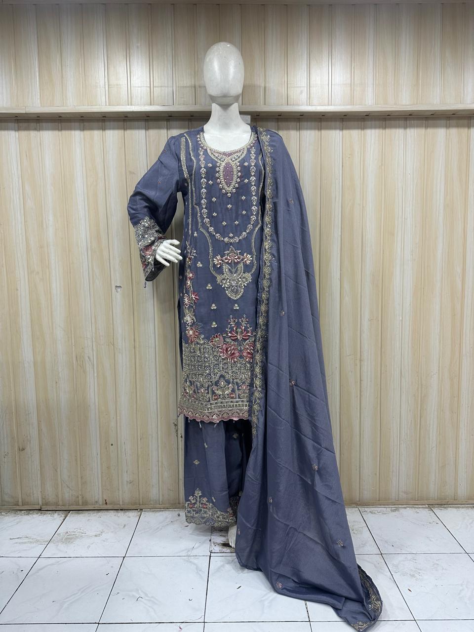 Mannequin wearing a traditional outfit with embroidered top and dark blue dupatta against a wooden panel background.
