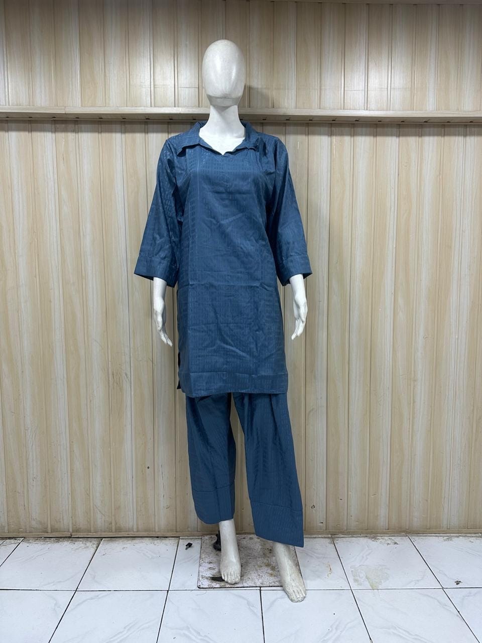 Mannequin wearing a blue outfit against a wooden panel background