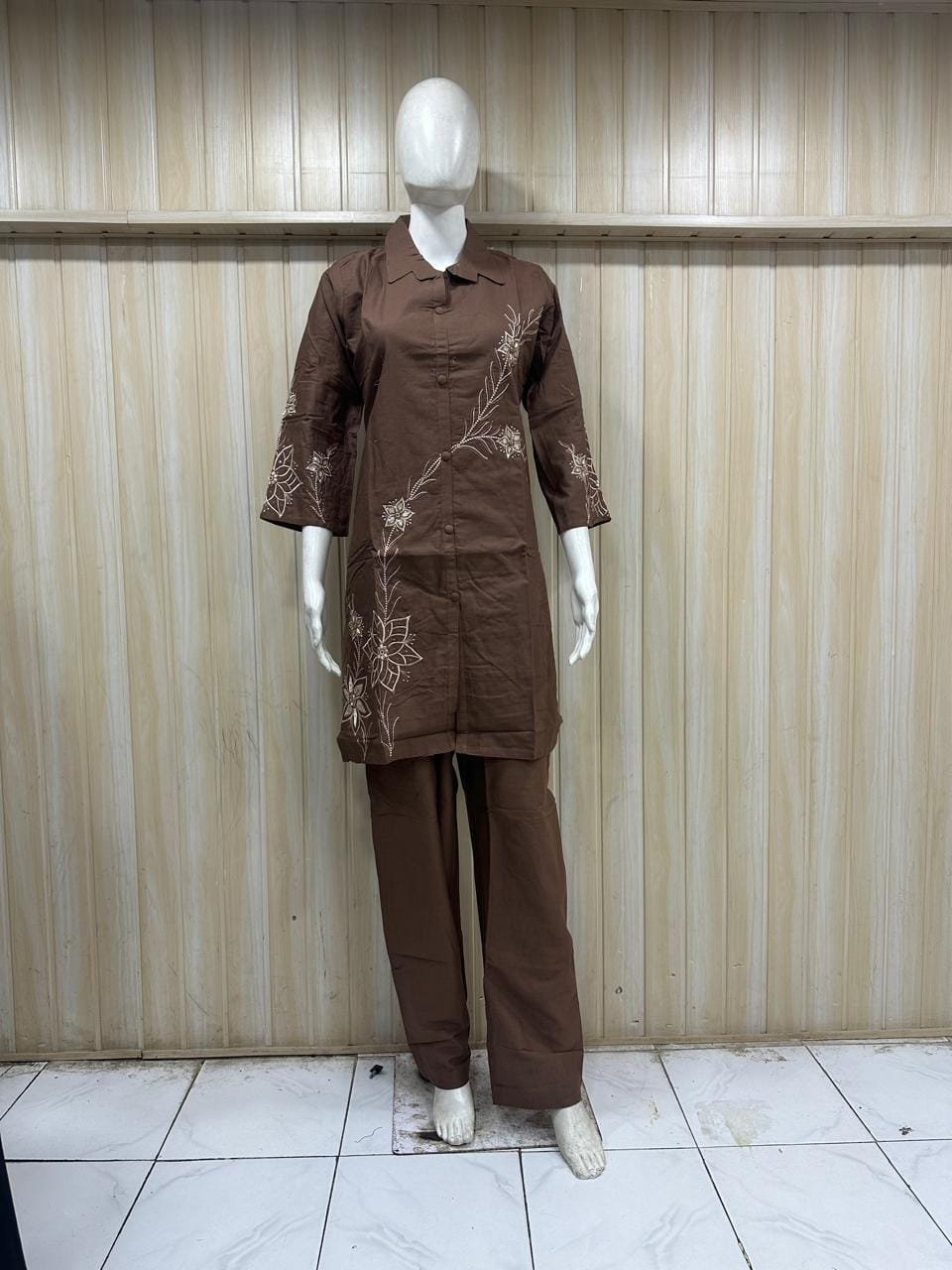 Brown outfit with floral embroidery on a mannequin against a striped