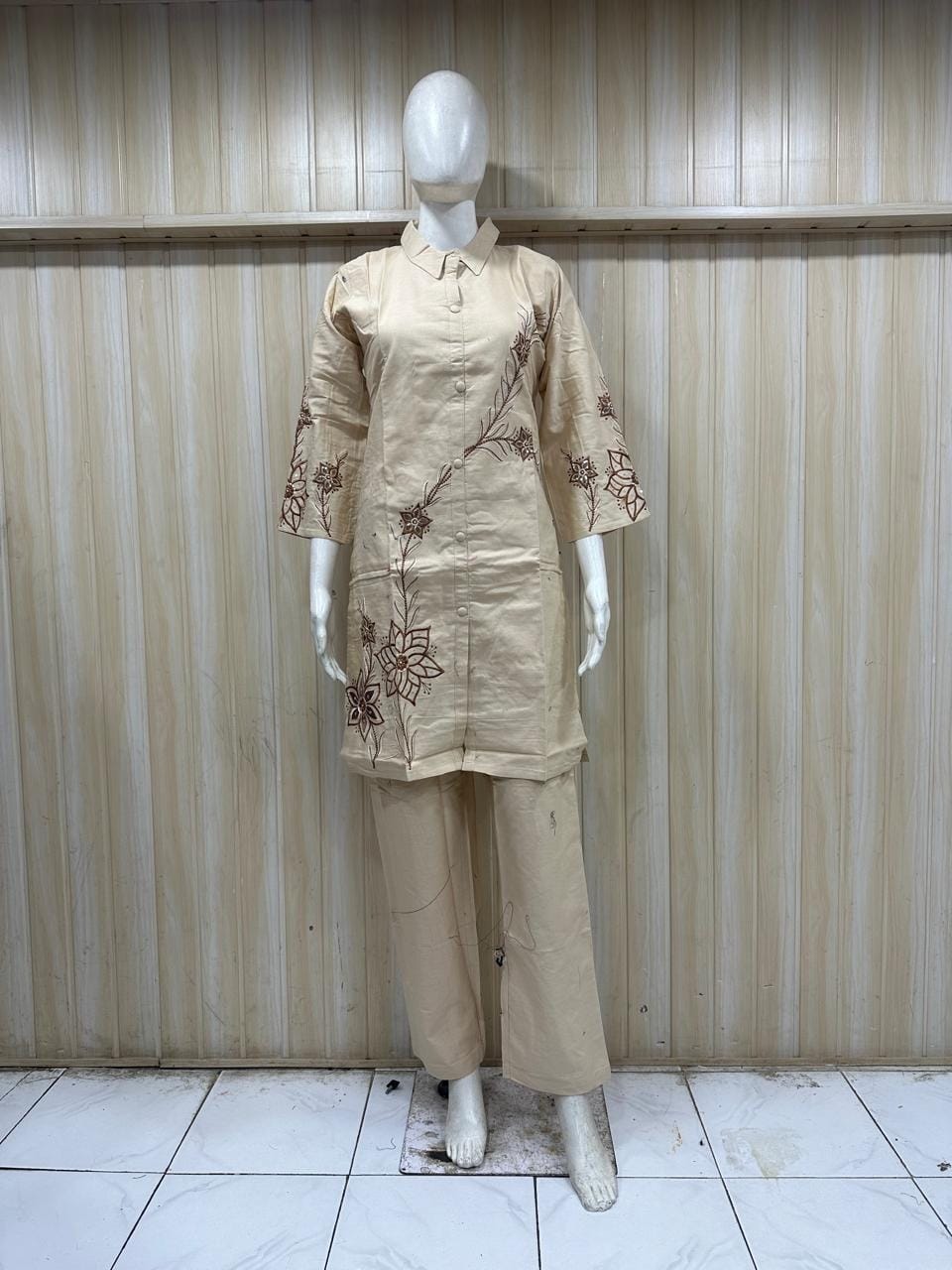 Mannequin wearing a beige outfit with floral embroidery against a striped