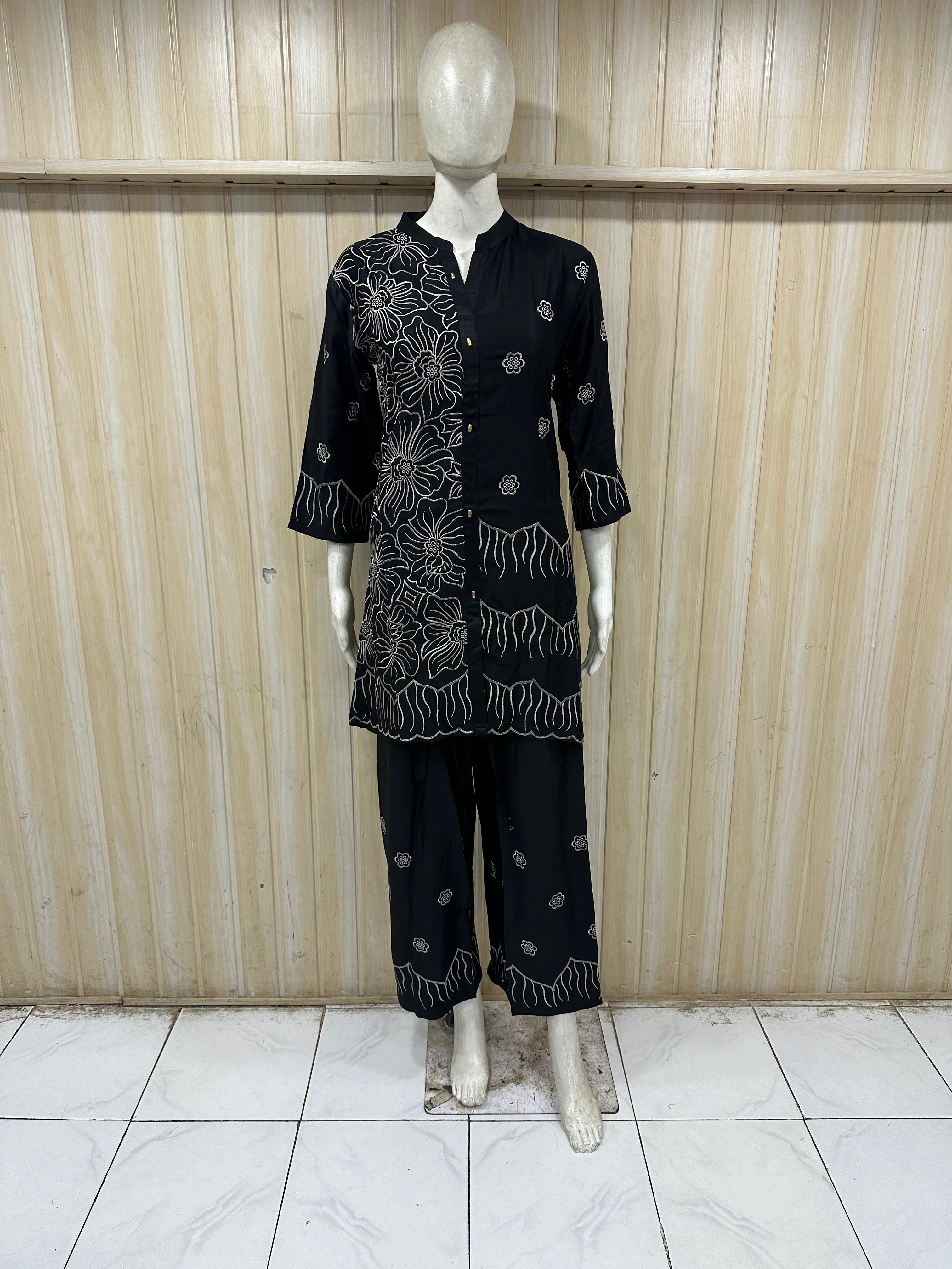 Mannequin wearing a black embroidered outfit against a wooden panel background