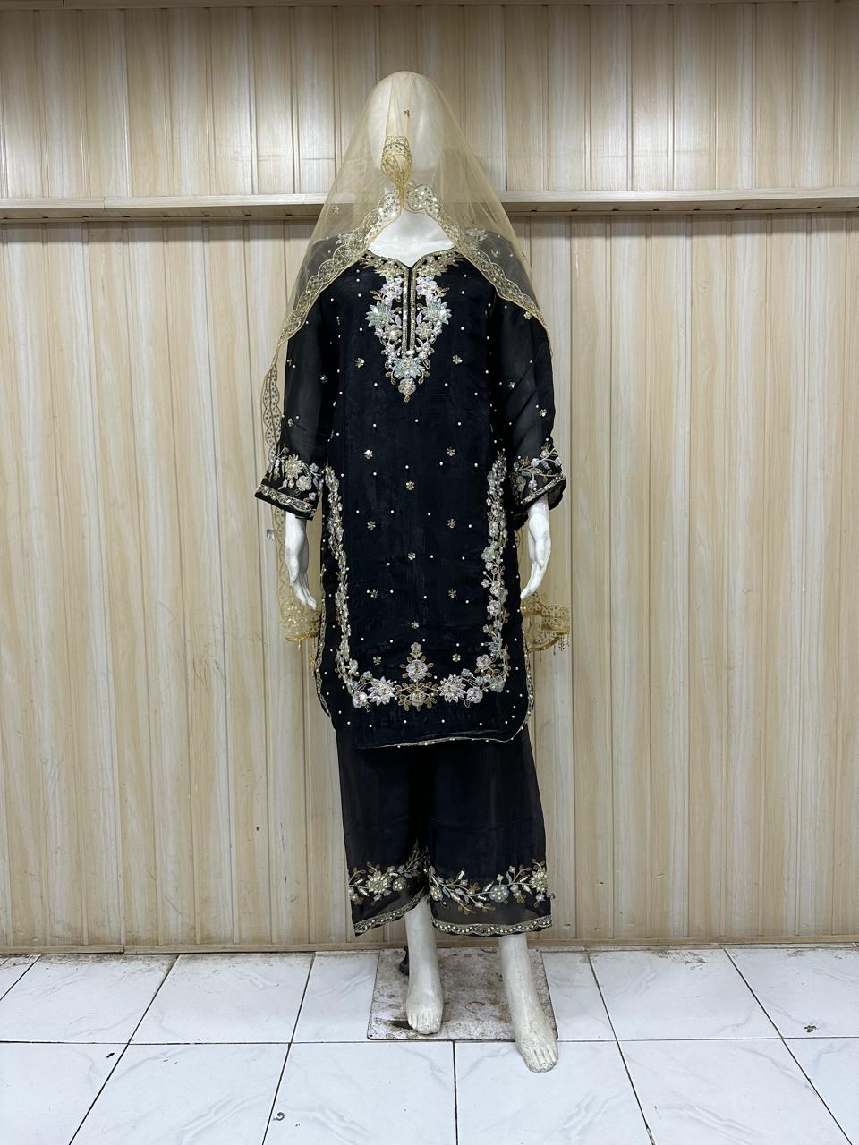 Black embroidered outfit with a veil on a mannequin against a striped