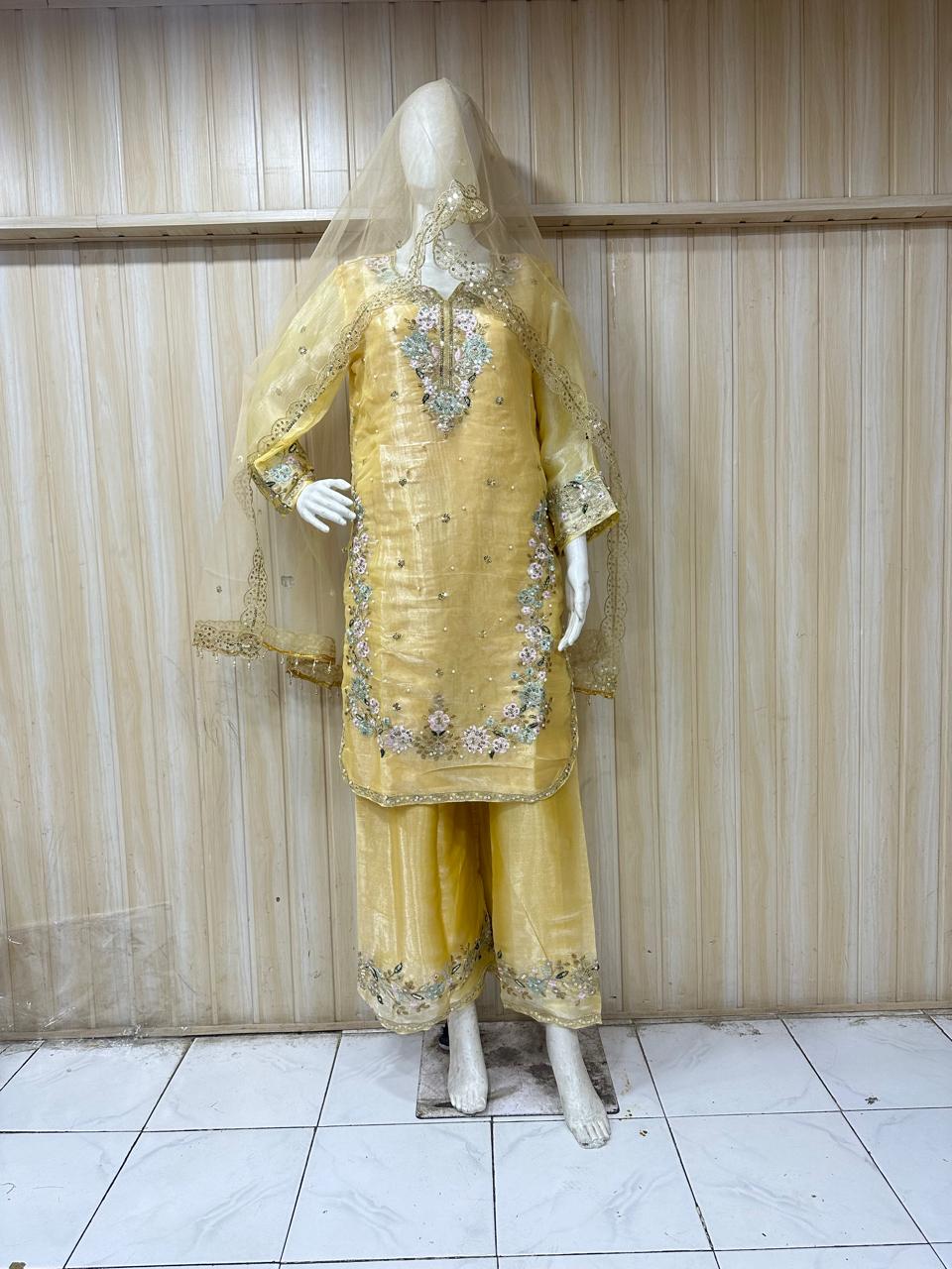 Mannequin wearing a yellow embroidered traditional outfit against a striped