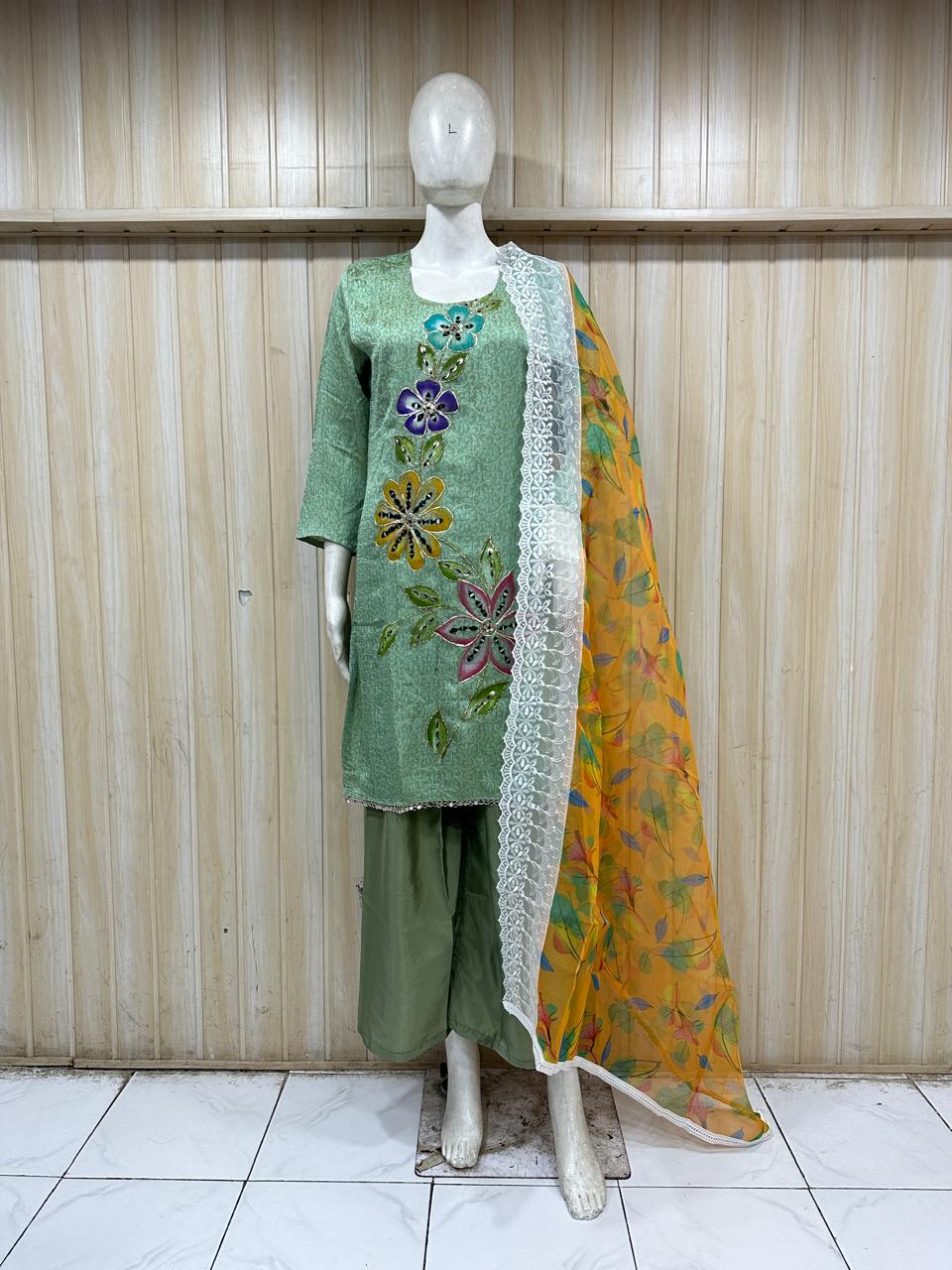 Mannequin wearing a green embroidered outfit with a yellow dupatta against a striped
