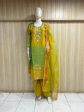 Mannequin wearing a yellow outfit with floral embroidery and a red floral dupatta against a wooden panel background.
