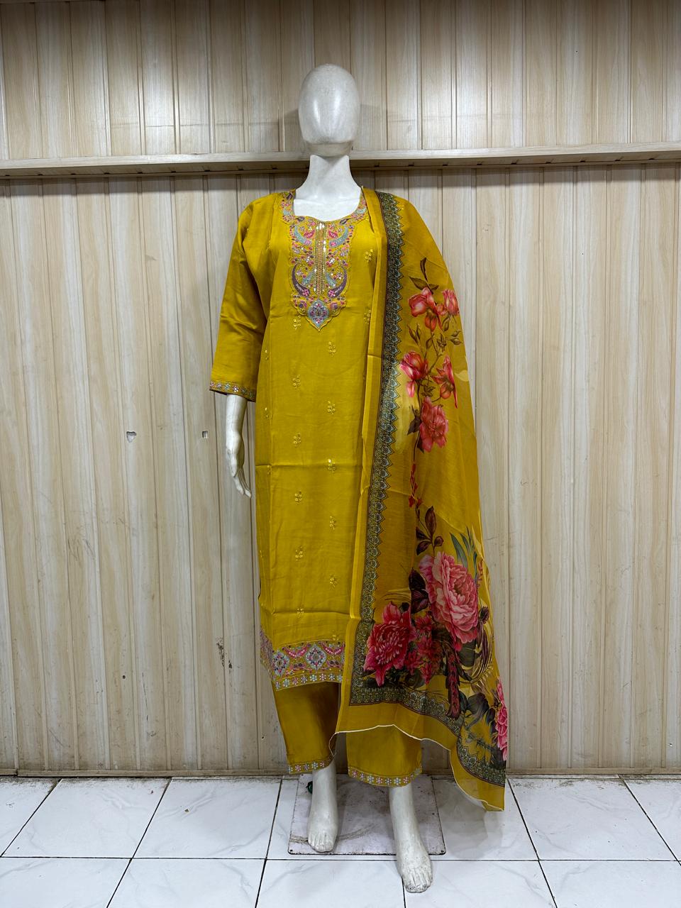 Yellow embroidered outfit with floral dupatta on a mannequin against a striped