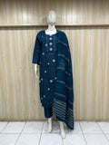 Mannequin wearing a blue embroidered outfit against a wooden panel background