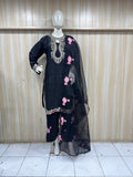 Black embroidered outfit with pink flowers on a mannequin against a wooden panel background.