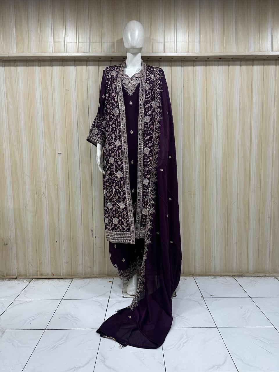 Mannequin wearing a dark purple embroidered outfit with a sheer dupatta against a wooden panel background.