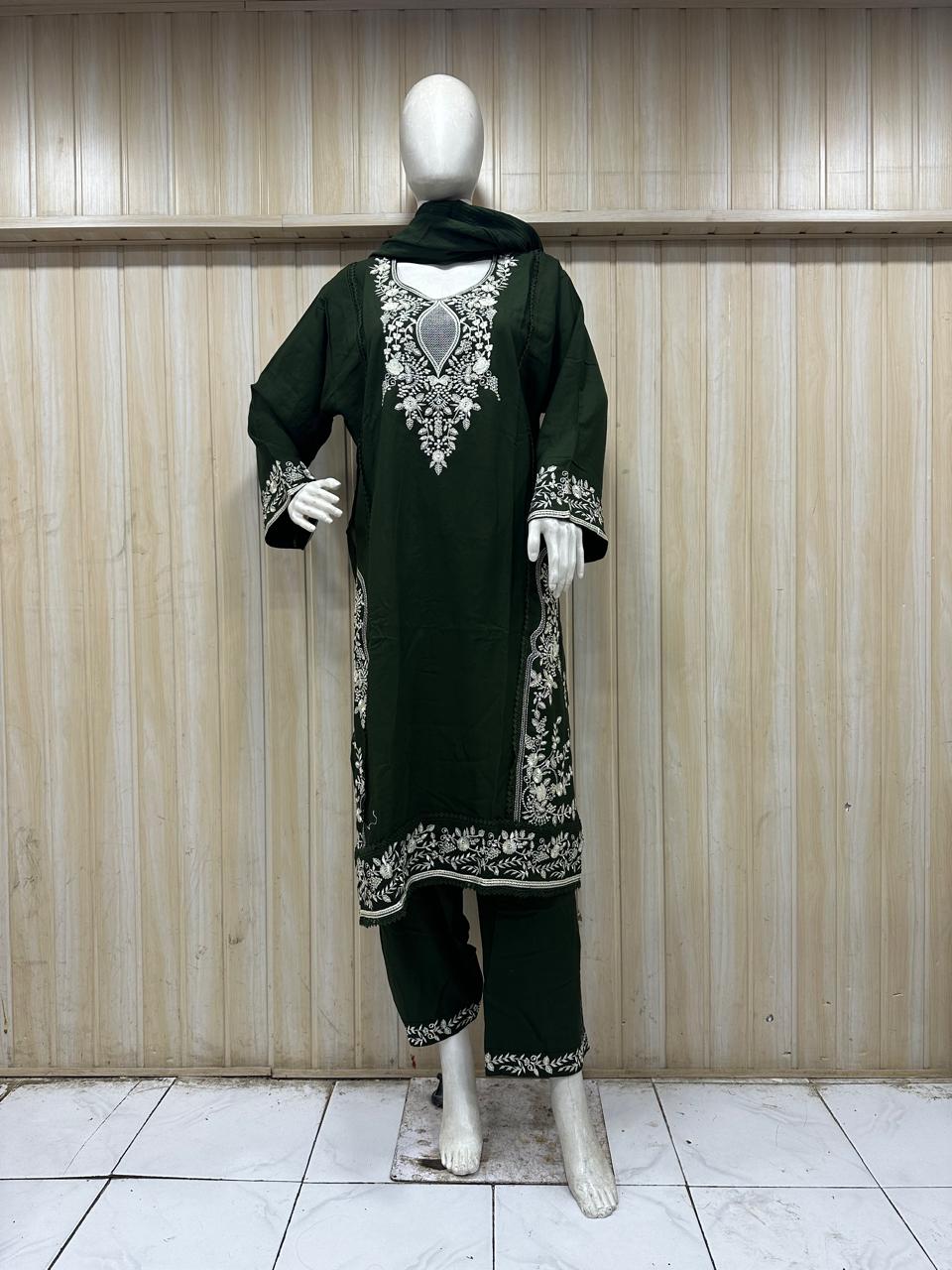 Mannequin wearing a dark green embroidered outfit with a sheer dupatta against a wooden panel background.