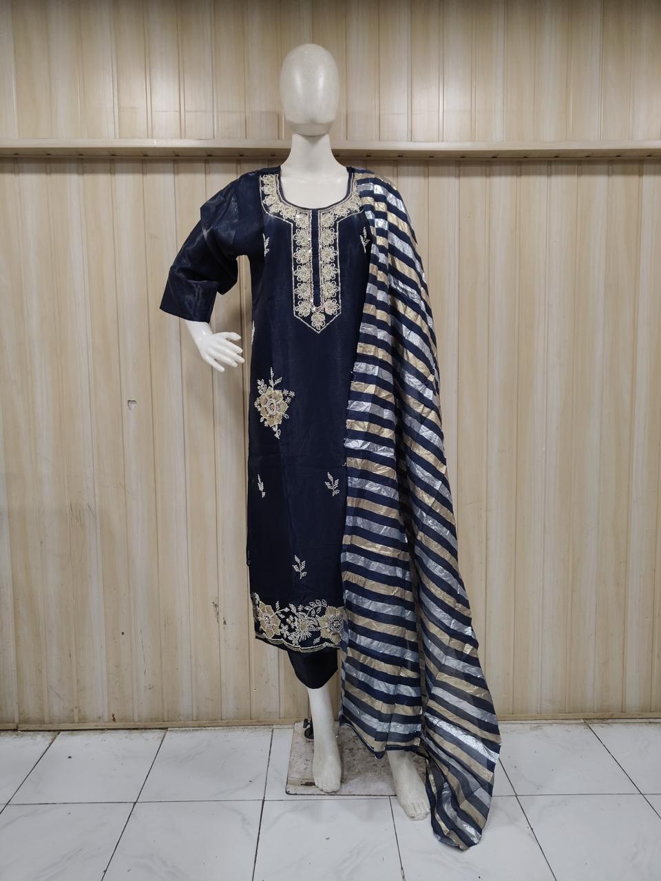 Mannequin wearing a black embroidered outfit with a sheer dupatta against a wooden panel background.