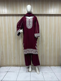 Maroon traditional outfit with intricate white embroidery on a mannequin against a wooden panel background.